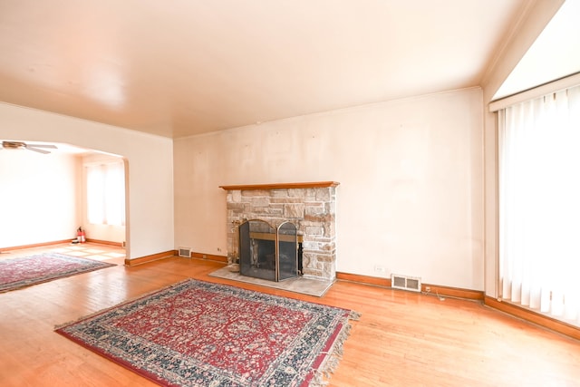 living room featuring crown molding, a stone fireplace, wood-type flooring, and plenty of natural light