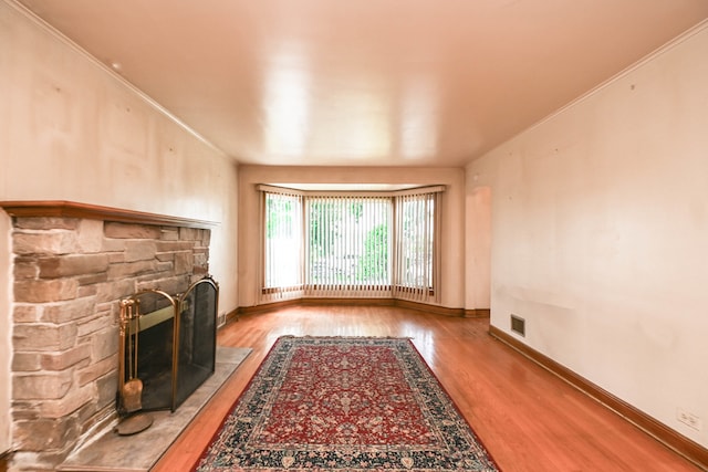 unfurnished living room with hardwood / wood-style flooring, ornamental molding, and a stone fireplace