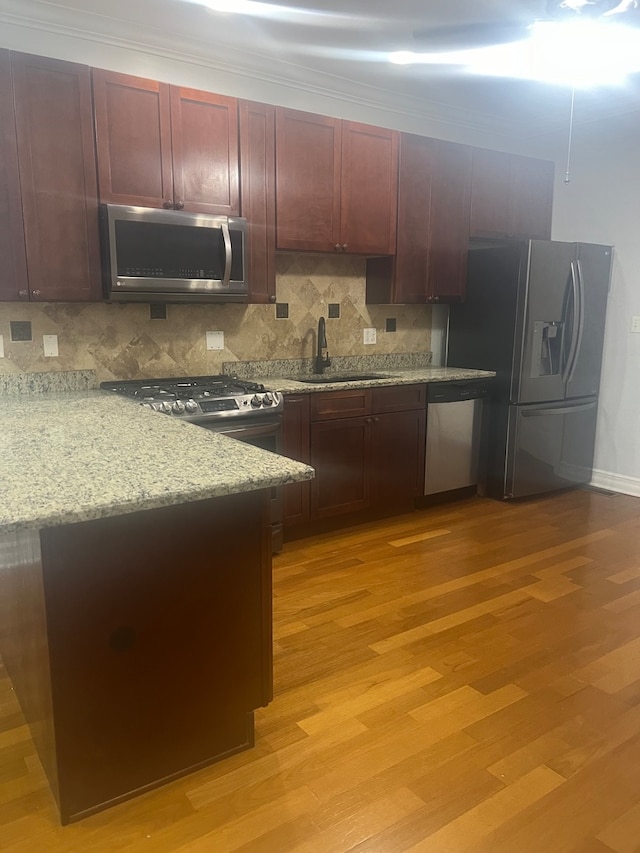 kitchen with stainless steel appliances, light wood-style floors, a sink, and backsplash