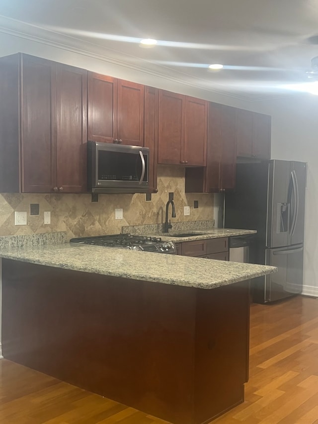 kitchen with stainless steel appliances, kitchen peninsula, decorative backsplash, and light hardwood / wood-style flooring