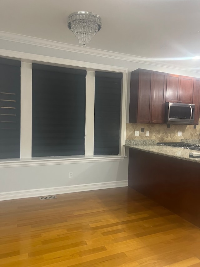 kitchen featuring crown molding, backsplash, light wood finished floors, stainless steel microwave, and an inviting chandelier