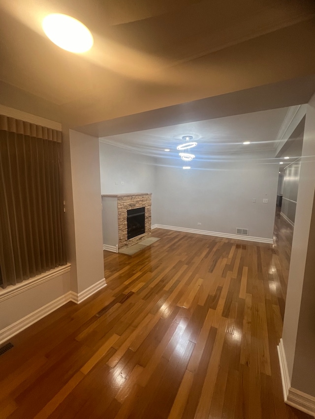 unfurnished living room with baseboards, visible vents, wood finished floors, and a stone fireplace