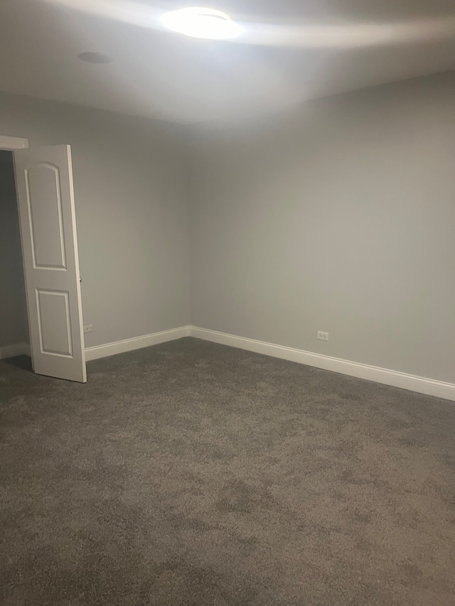 spare room with dark carpet and baseboards