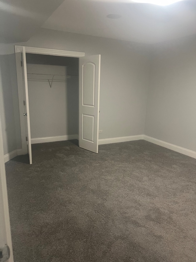 unfurnished bedroom featuring a closet, dark carpet, and baseboards