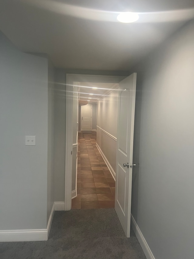 corridor featuring dark colored carpet and baseboards