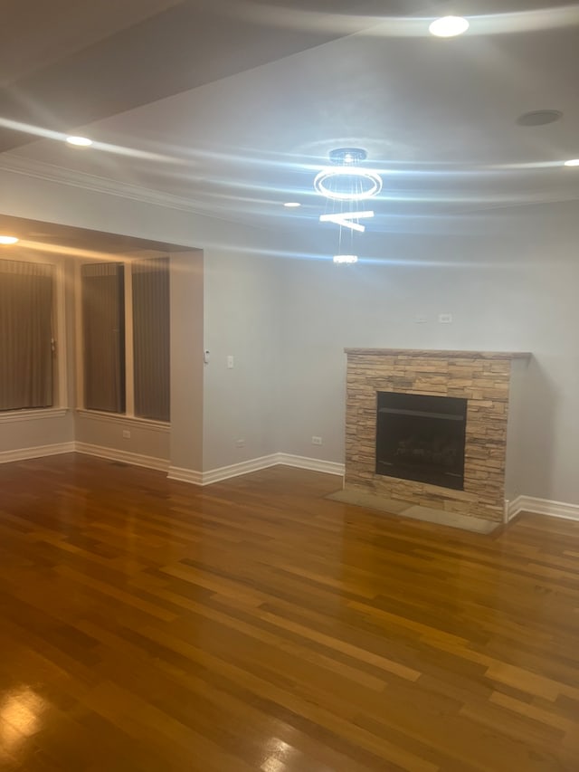 unfurnished living room with a stone fireplace, wood finished floors, and baseboards