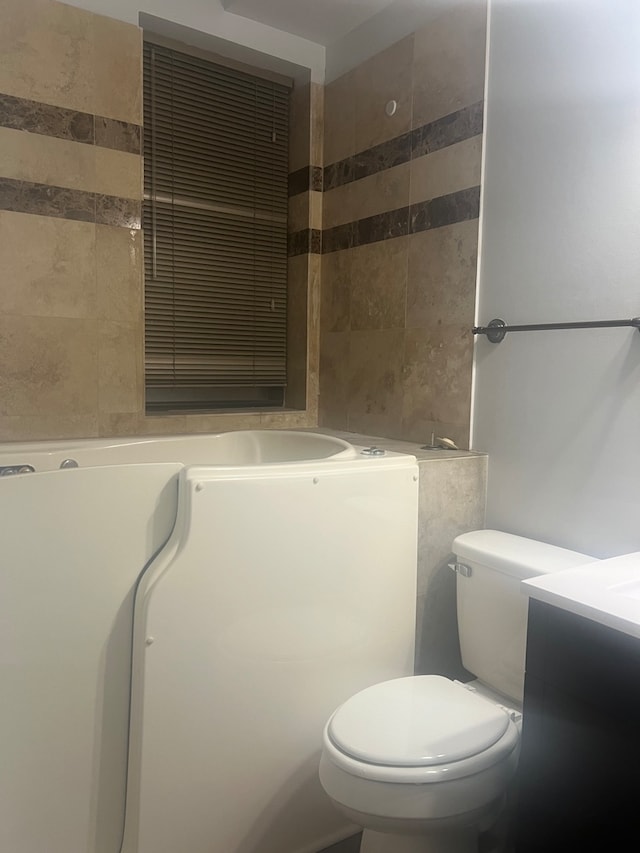 bathroom with toilet, tile walls, and vanity