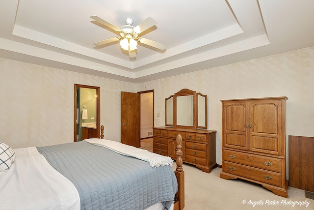 carpeted bedroom featuring a raised ceiling, ensuite bath, and ceiling fan