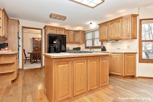 kitchen with a center island, light hardwood / wood-style floors, black fridge with ice dispenser, and stainless steel gas cooktop