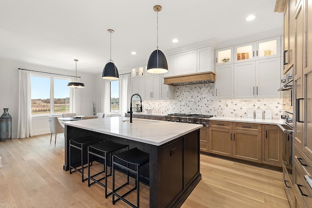 kitchen with a kitchen island with sink, light hardwood / wood-style flooring, white cabinets, and light stone countertops