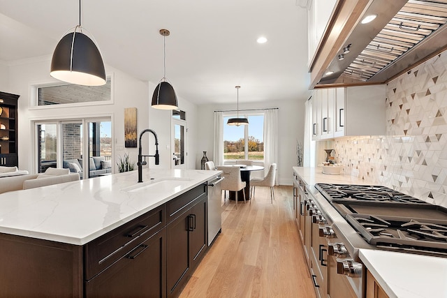 kitchen featuring sink, wall chimney exhaust hood, light hardwood / wood-style flooring, an island with sink, and pendant lighting