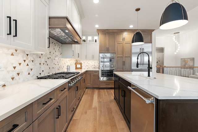 kitchen featuring light wood-type flooring, stainless steel appliances, sink, white cabinets, and hanging light fixtures