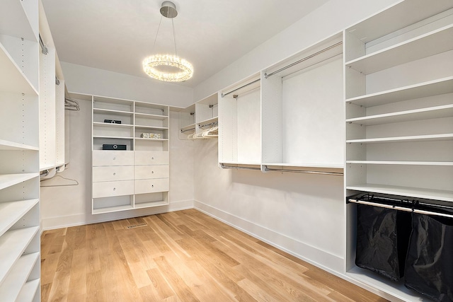 spacious closet featuring an inviting chandelier and light wood-type flooring