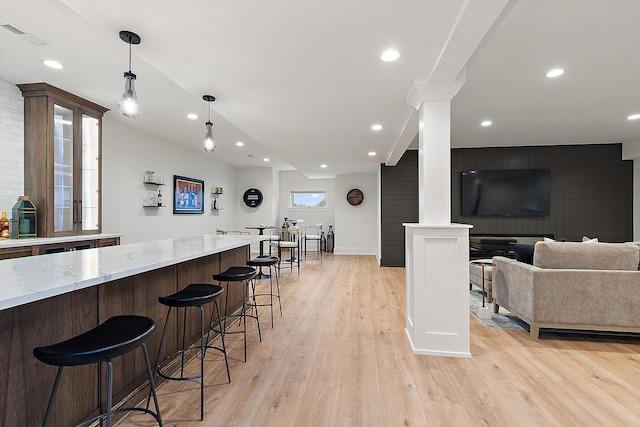 kitchen featuring a breakfast bar area, light stone counters, hanging light fixtures, and light hardwood / wood-style floors