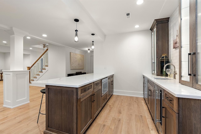 kitchen with sink, hanging light fixtures, light stone counters, light hardwood / wood-style flooring, and kitchen peninsula