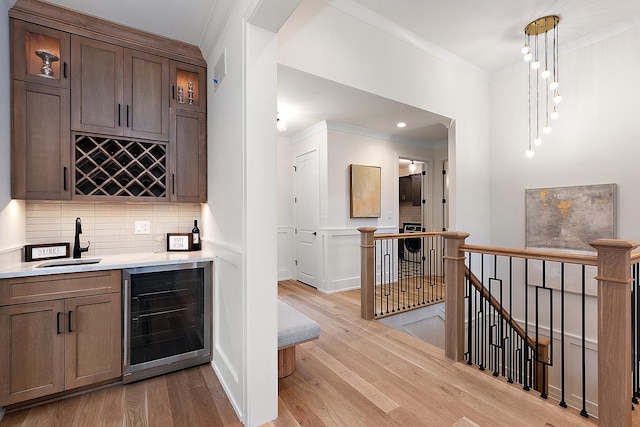 bar with crown molding, sink, light hardwood / wood-style flooring, wine cooler, and hanging light fixtures