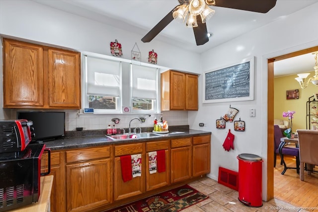 kitchen featuring decorative backsplash, light wood-type flooring, ceiling fan with notable chandelier, and sink