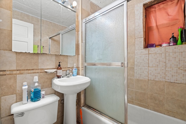 full bathroom with combined bath / shower with glass door, tile walls, sink, and toilet