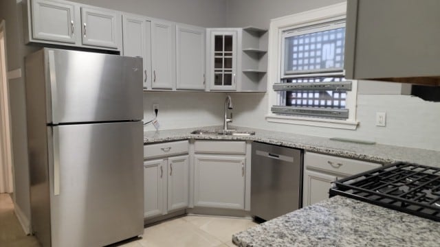 kitchen with appliances with stainless steel finishes, white cabinetry, sink, and light stone counters