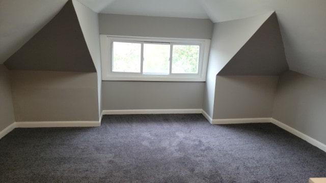 bonus room with dark carpet and vaulted ceiling