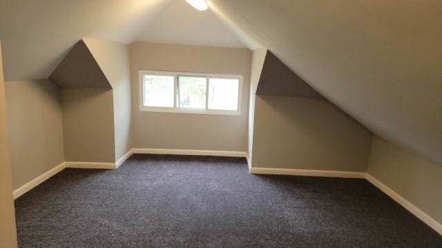 additional living space with dark colored carpet and vaulted ceiling