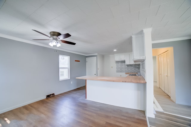 kitchen with light wood-type flooring, kitchen peninsula, tasteful backsplash, and white cabinetry