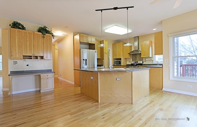 kitchen featuring stainless steel appliances, a kitchen island with sink, wall chimney range hood, decorative light fixtures, and light hardwood / wood-style flooring