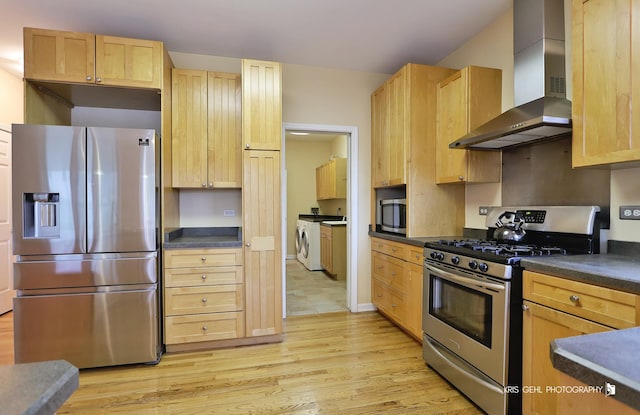 kitchen featuring light brown cabinets, wall chimney exhaust hood, light hardwood / wood-style flooring, washer and dryer, and appliances with stainless steel finishes