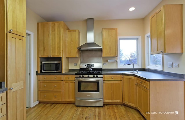 kitchen featuring light wood-type flooring, stainless steel appliances, sink, wall chimney range hood, and light brown cabinets