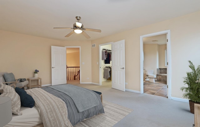 bedroom featuring a walk in closet, light colored carpet, ceiling fan, connected bathroom, and a closet