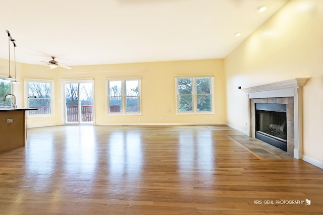 unfurnished living room featuring a tile fireplace, light hardwood / wood-style flooring, ceiling fan, and sink