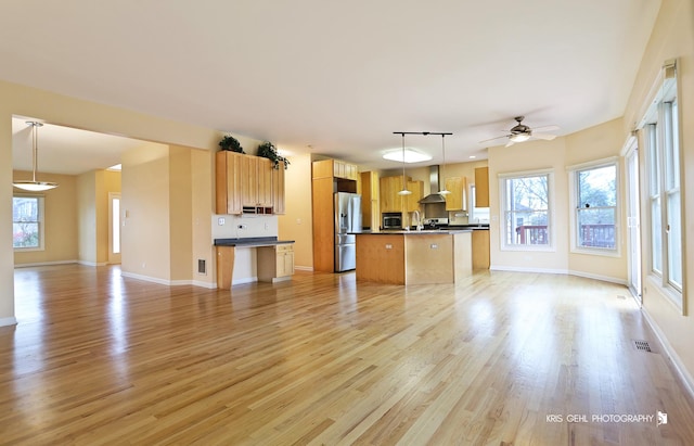 kitchen with decorative light fixtures, light hardwood / wood-style flooring, a healthy amount of sunlight, and wall chimney range hood