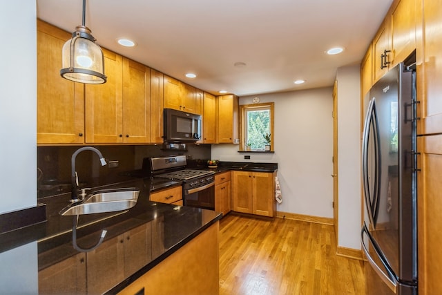 kitchen featuring appliances with stainless steel finishes, dark stone countertops, light hardwood / wood-style flooring, decorative light fixtures, and sink