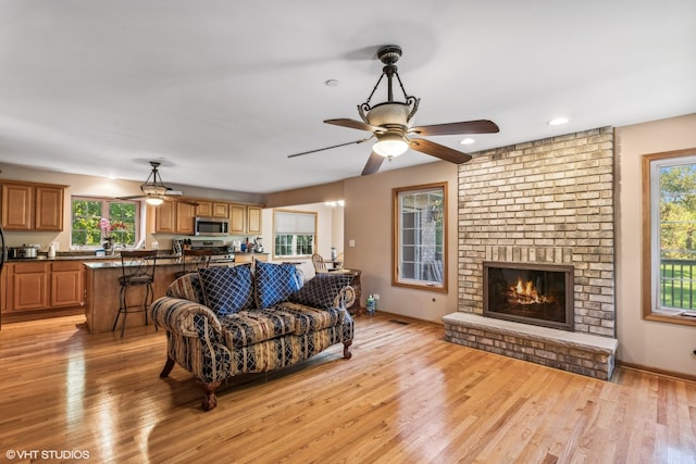 living room featuring a fireplace, ceiling fan, and light wood-type flooring