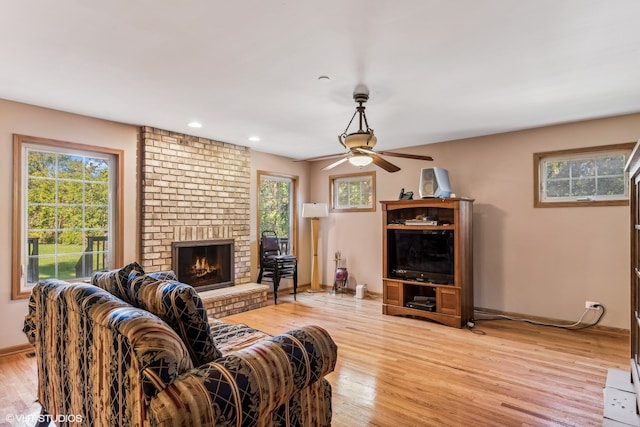 living room featuring light wood-type flooring, ceiling fan, and a fireplace