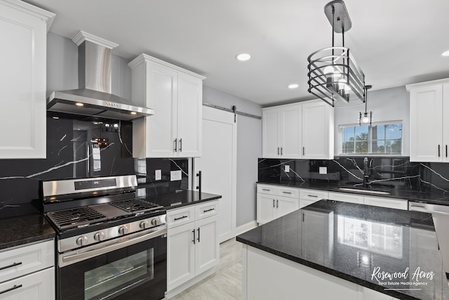 kitchen with gas range, white cabinets, wall chimney exhaust hood, pendant lighting, and a barn door