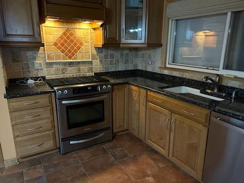 kitchen with decorative backsplash, sink, stainless steel appliances, and dark stone countertops