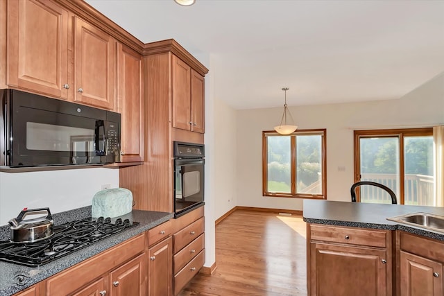 kitchen with black appliances, decorative light fixtures, and light wood-type flooring