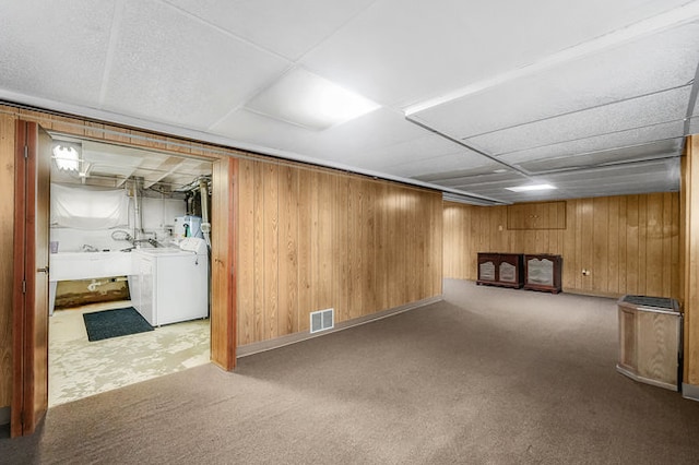 basement featuring wooden walls, water heater, carpet floors, and sink