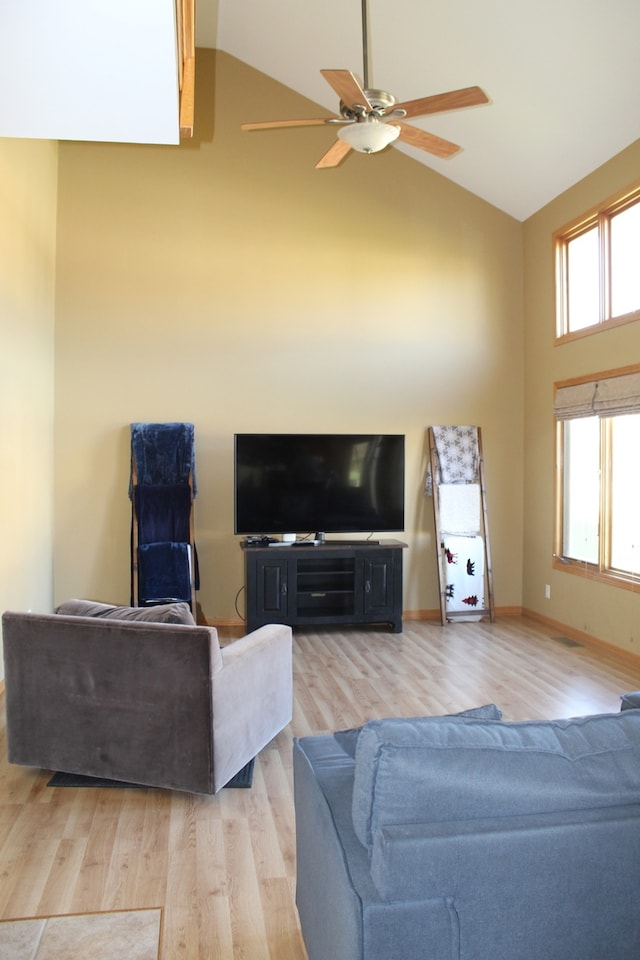 living room featuring a skylight, high vaulted ceiling, light wood-type flooring, and ceiling fan