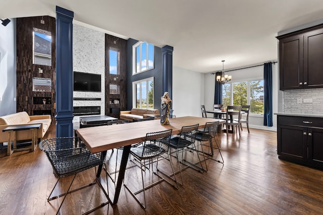 dining area with a stone fireplace, dark hardwood / wood-style floors, a chandelier, and ornate columns