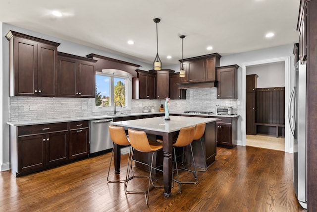 kitchen with appliances with stainless steel finishes, dark hardwood / wood-style flooring, decorative light fixtures, and a kitchen island