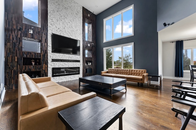 living room with a wealth of natural light, a high ceiling, a stone fireplace, and hardwood / wood-style flooring