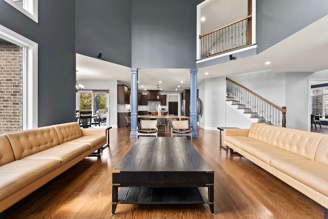 living room with hardwood / wood-style floors, a high ceiling, a notable chandelier, and decorative columns