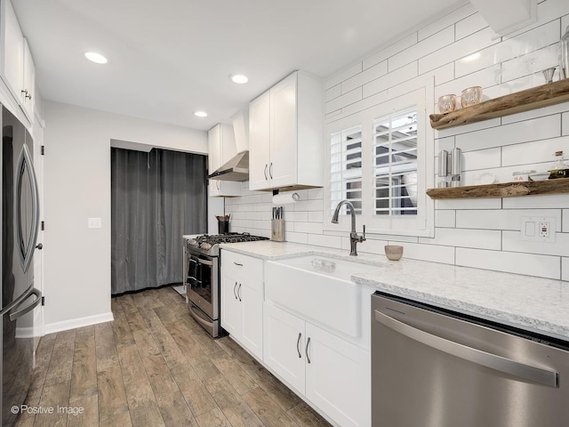 kitchen with appliances with stainless steel finishes, tasteful backsplash, exhaust hood, hardwood / wood-style flooring, and white cabinetry