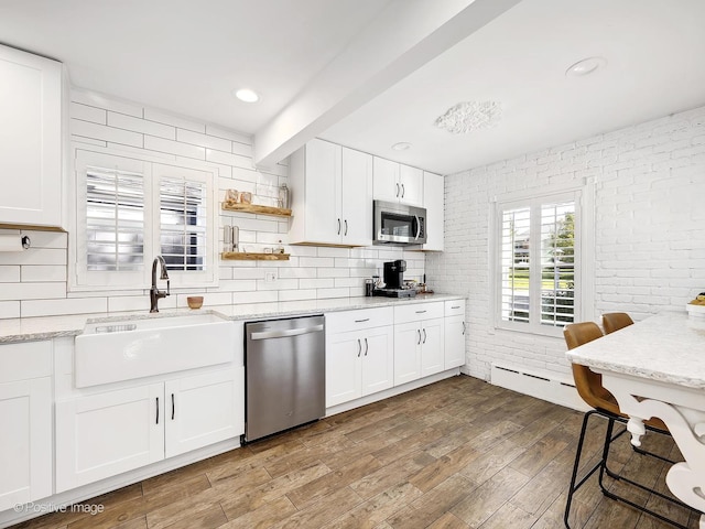 kitchen with sink, light hardwood / wood-style flooring, light stone countertops, appliances with stainless steel finishes, and white cabinetry