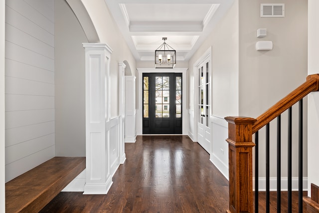 entryway featuring a raised ceiling, dark hardwood / wood-style flooring, an inviting chandelier, decorative columns, and ornamental molding