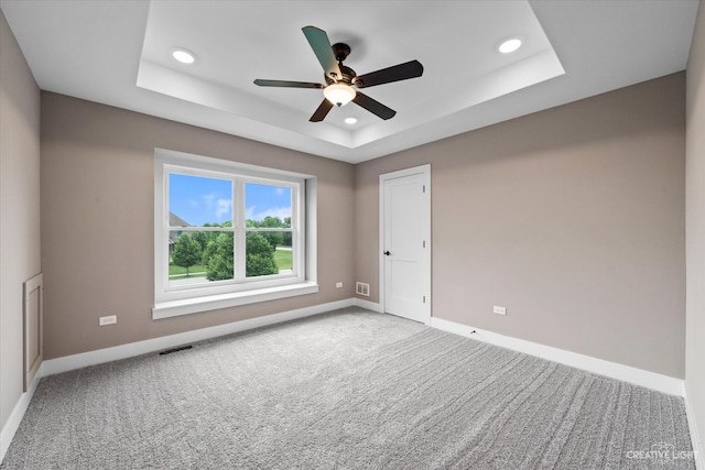 carpeted spare room featuring a tray ceiling and ceiling fan