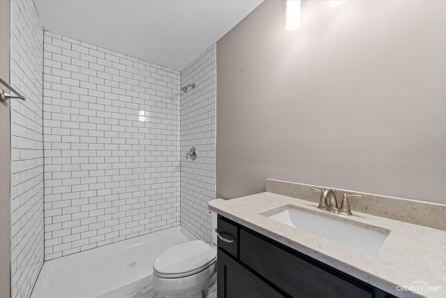 bathroom with a tile shower, vanity, and toilet