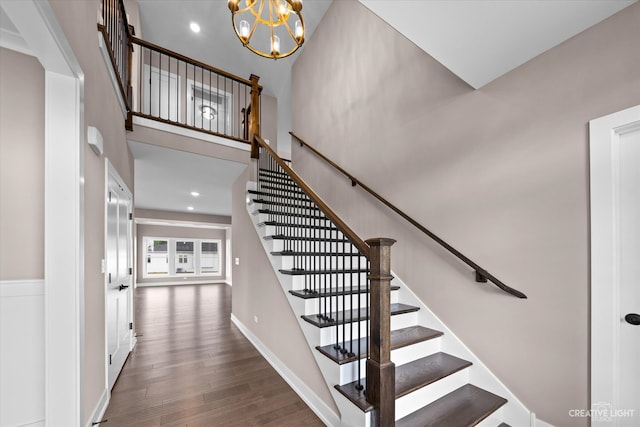 stairway with wood-type flooring, an inviting chandelier, and a high ceiling